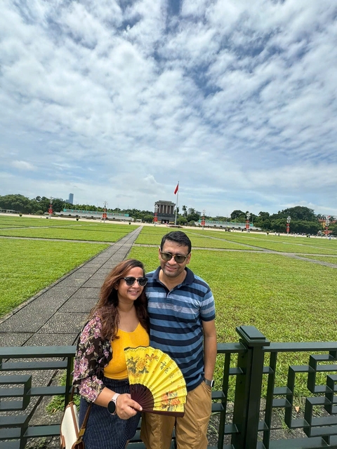 A couple taking a selfie in front of a grass field and a flag in the distance.