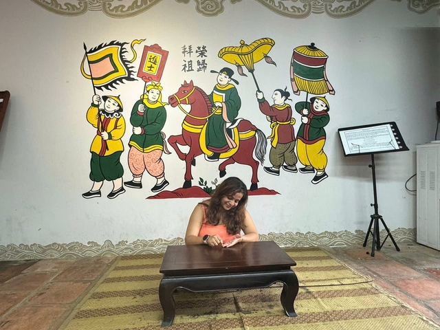 A woman sitting at a table in front of a colorful mural depicting historical figures.