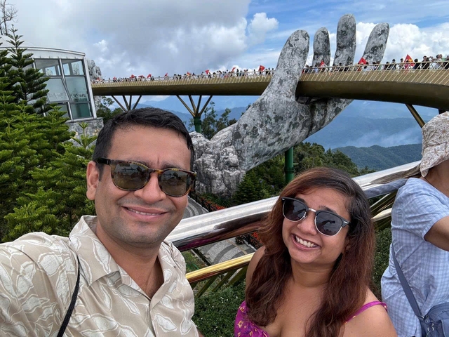       A couple posing in front of a bridge with large stone hands holding it.
  