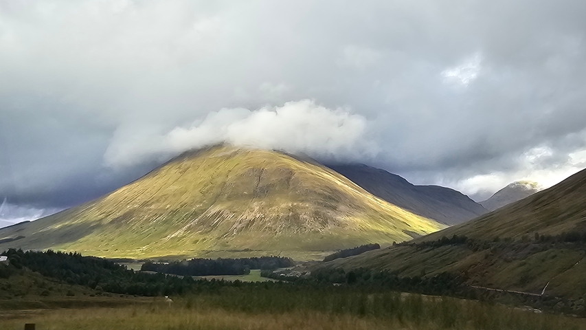 A mountain partially covered by clouds under a dramatic sky.