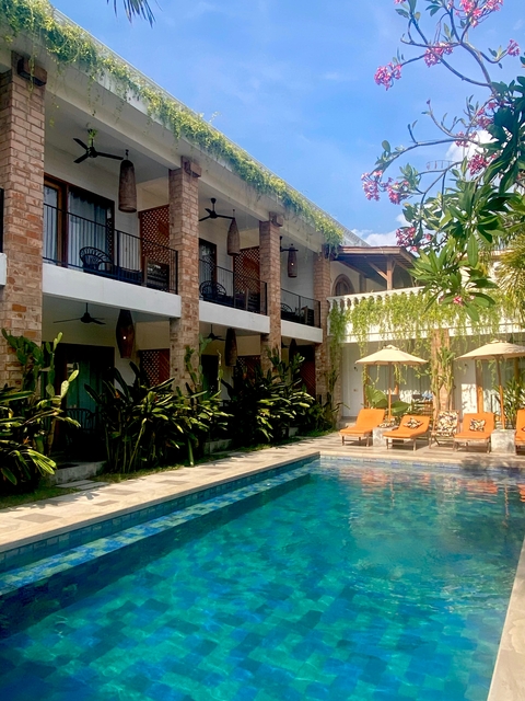       Exterior view of a hotel with a pool and lush greenery
  