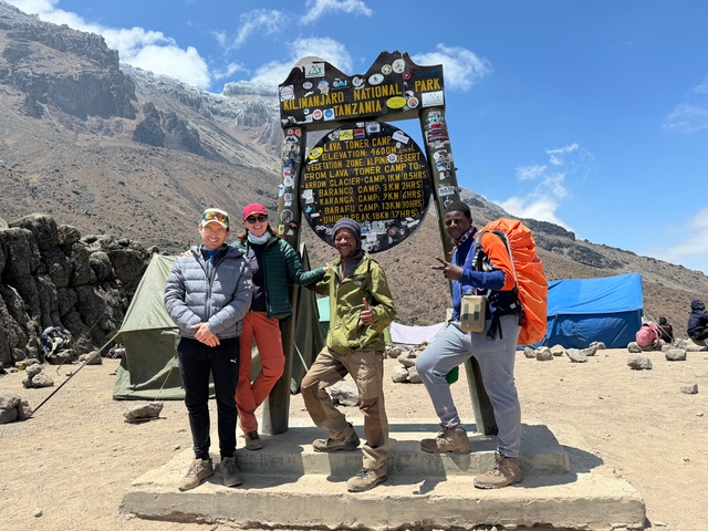 People posing under the Kilimanjaro National Park sign.