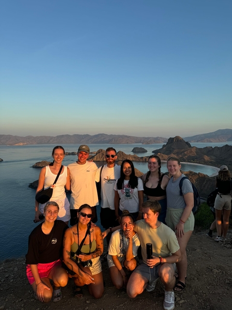 Group of people posing in front of rolling hills and a bay at sunset.