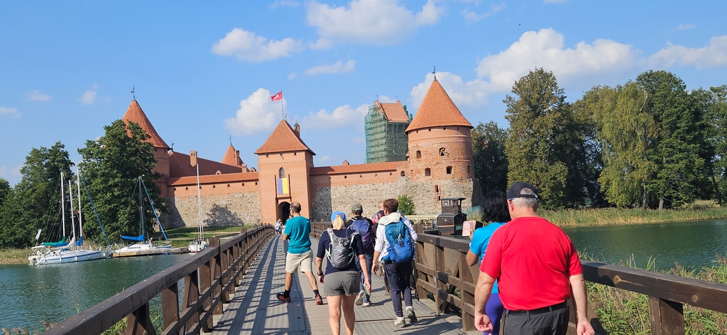       People walking towards a castle on a wooden bridge.
  