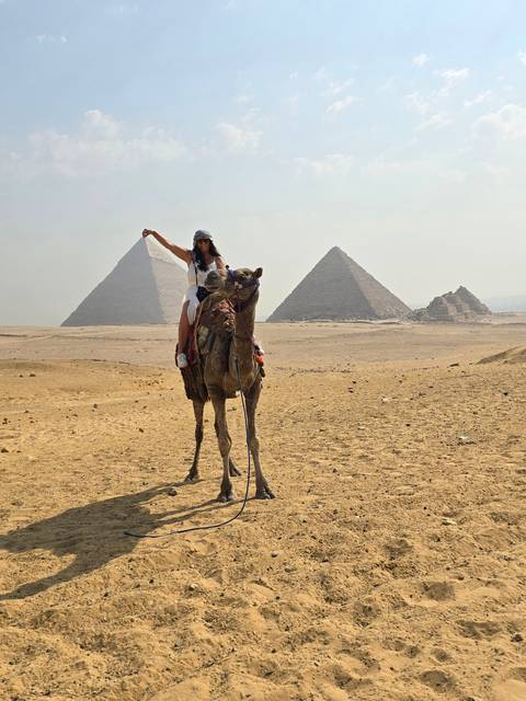 Woman on camel with pyramids in the background.