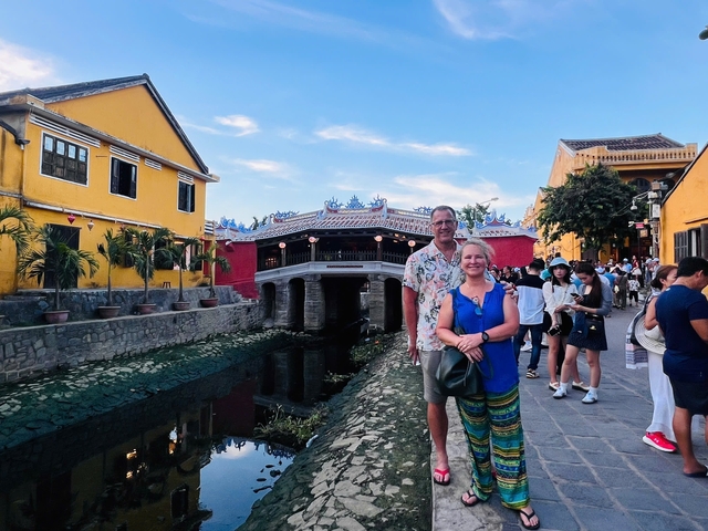 Couple posing by a canal in front of a red bridge with tourists.