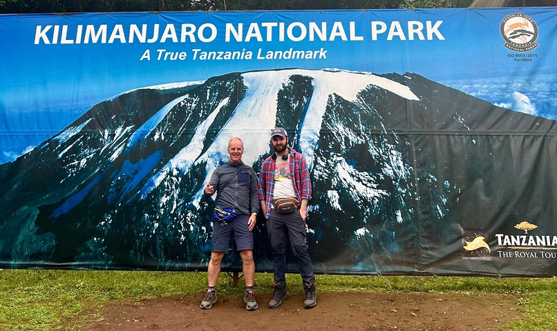 Two people posing with a Kilimanjaro National Park sign.