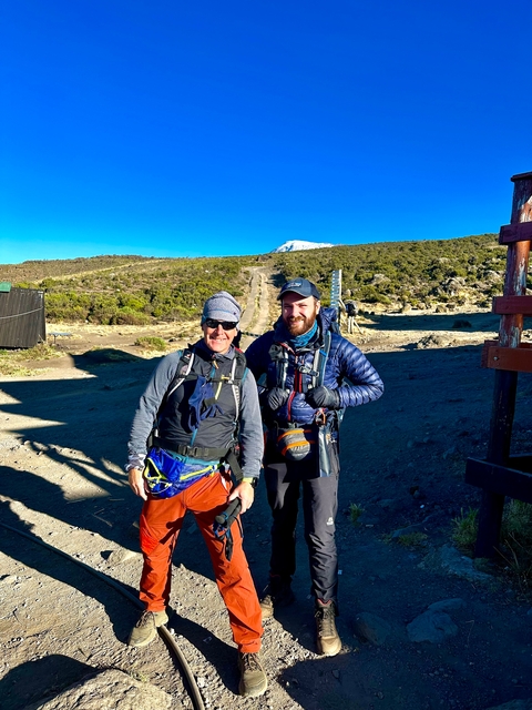 Two hikers posing on a mountain path with Kilimanjaro in the background.