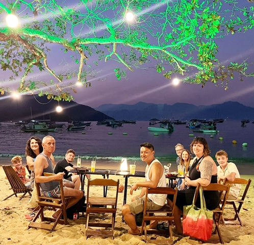 Group dining at the beach with boats in the background.