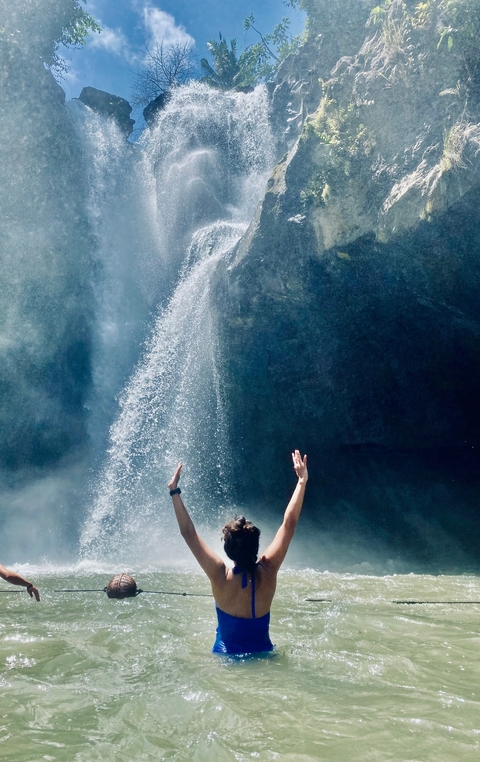 Person with outstretched arms in front of a waterfall.