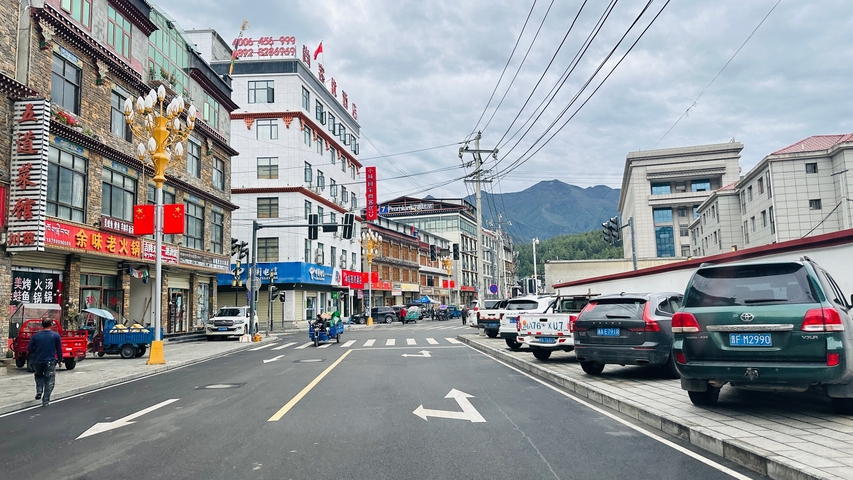 Urban street with cars and buildings, cloudy sky.