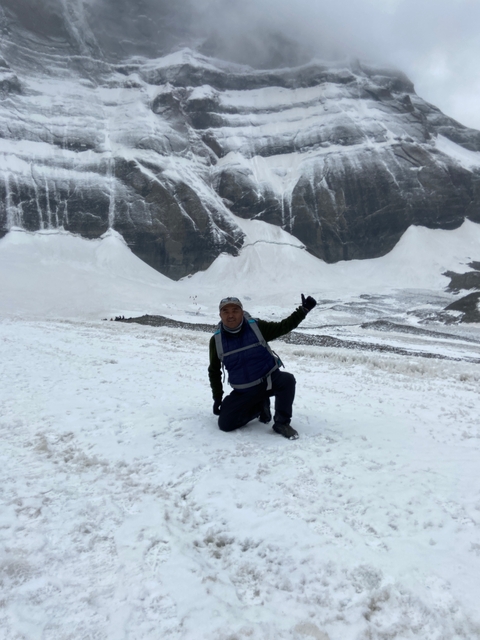 Person kneeling in snow pointing towards the mountain.