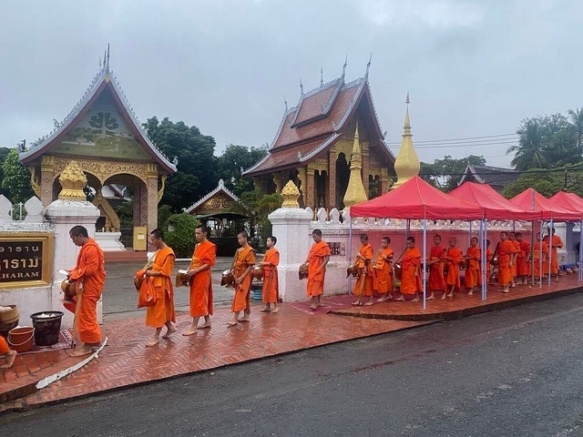       Procession of monks in orange robes in front of temples.
  