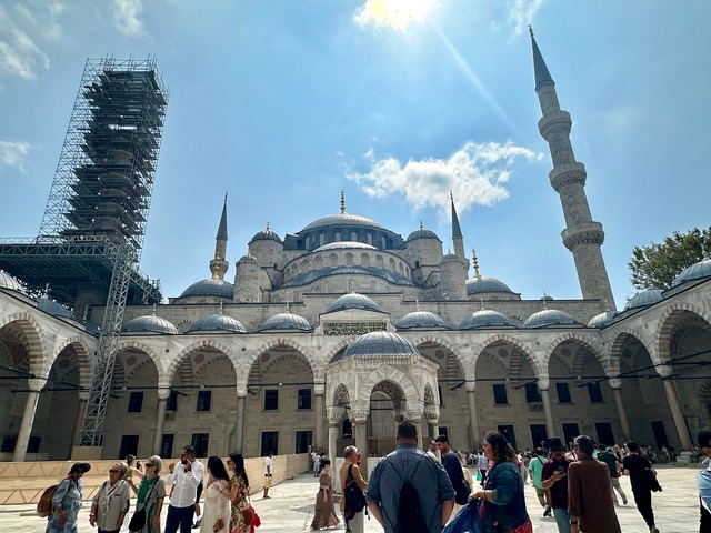 Historic mosque with domes and a scaffolded minaret.