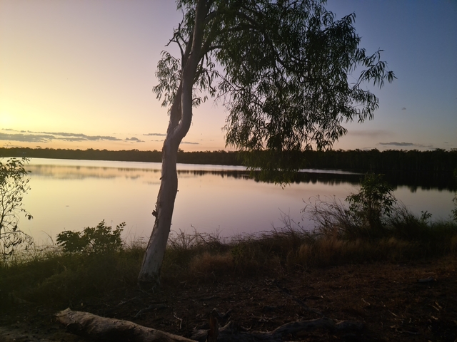 Calm lake at sunset with trees on the horizon.