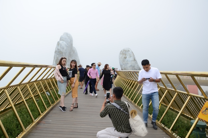 Tourists on a bridge taking photos in a foggy setting.