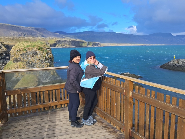       Two people standing on a wooden platform with ocean views.
  