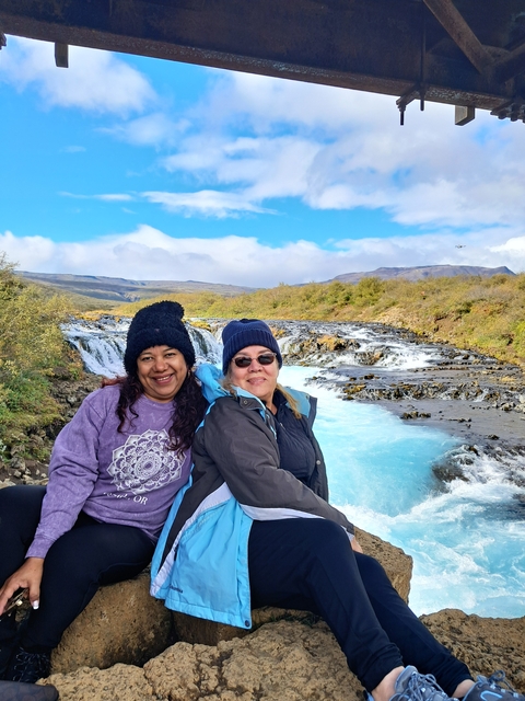       Two people smiling in front of a scenic waterfall.
  