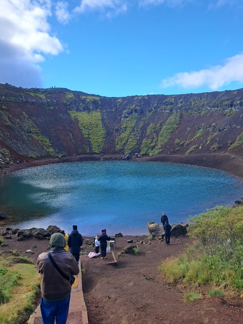       A wide view of a crater lake with lush green surroundings.
  