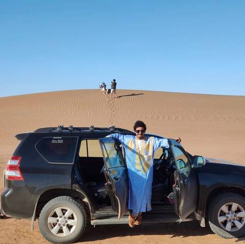 Man posing with a jeep at a desert site.