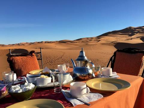 Outdoor table set for a meal, overlooking desert dunes.