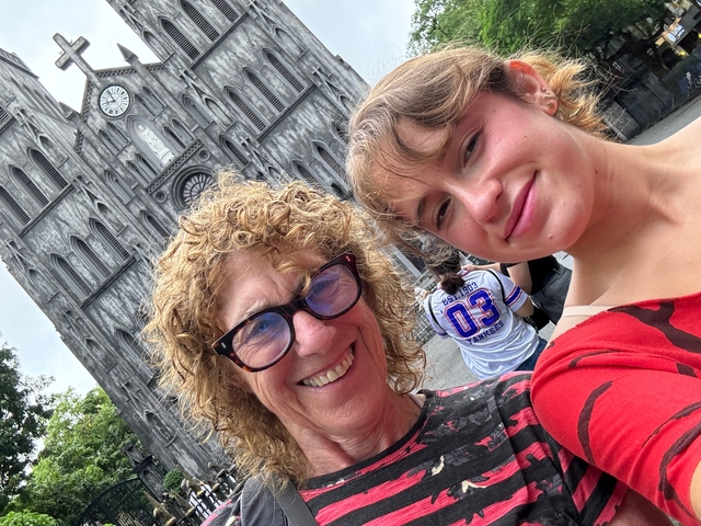 Two women posing in front of a gothic-style building, one wearing red clothing.