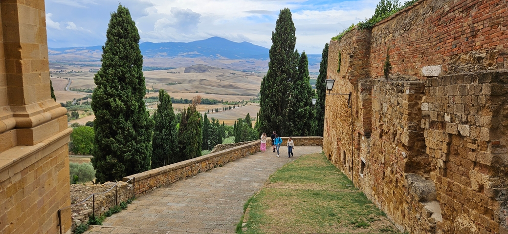 Walkway with stone walls and cypress trees overlooking a scenic landscape.