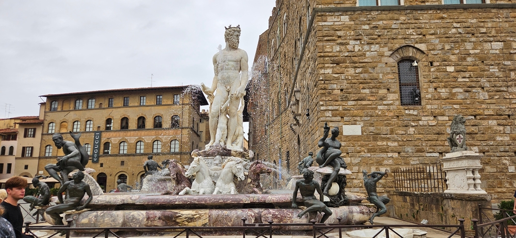       Fountain with statues surrounded by historic architecture.
  