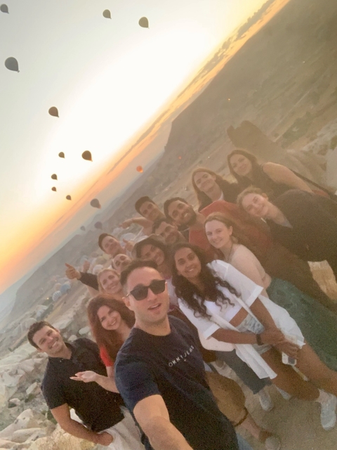 Group of friends taking a selfie with hot air balloons in the background.