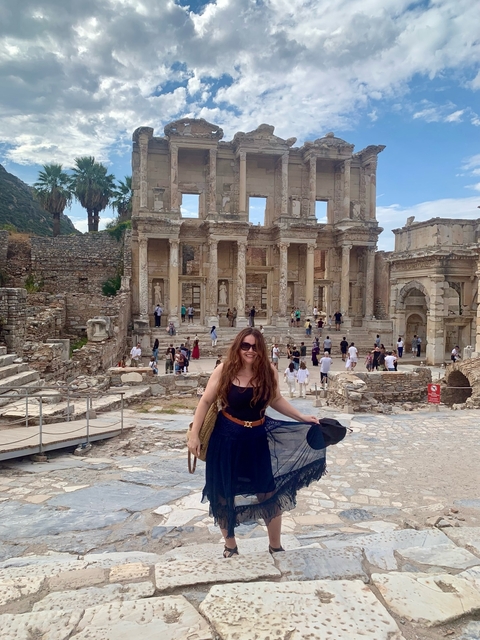 Woman posing in front of ancient ruins with people in the background.