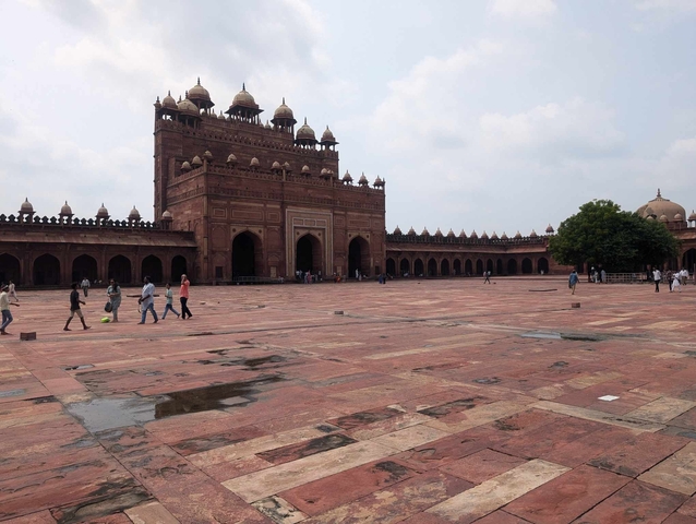       Tourists walking across a large courtyard in front of an ancient building.
  