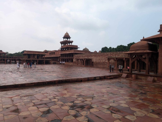       A spacious courtyard with ancient buildings and tourists.
  