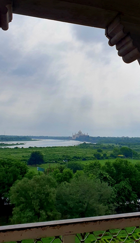       A distant view of the Taj Mahal across a river.
  