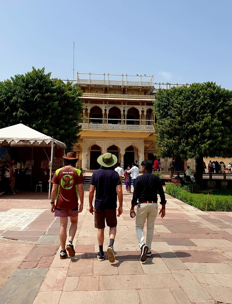       Three men walking towards a traditional building set among green trees.
  