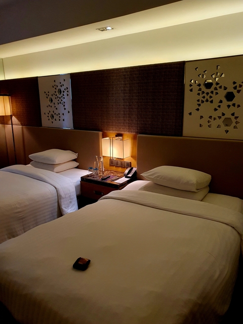       A hotel room with twin beds, dimly lit.
  