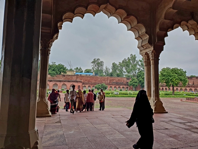       People walking in the courtyard of a red fort with arches.
  