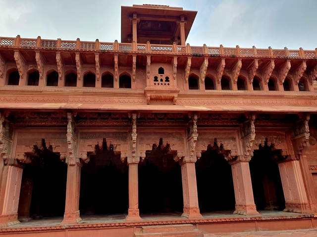       Facade of an ancient red fort with ornate arches and windows.
  
