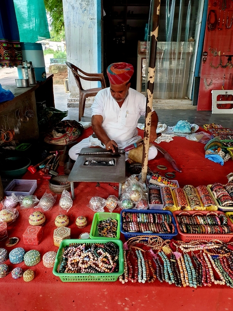       A vendor sitting with displayed items on a red mat.
  