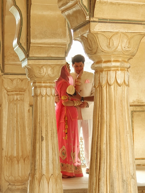      A couple in traditional dress standing by ornately carved pillars.
  