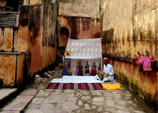       A man with traditional dolls and instruments in a narrow alley.
  