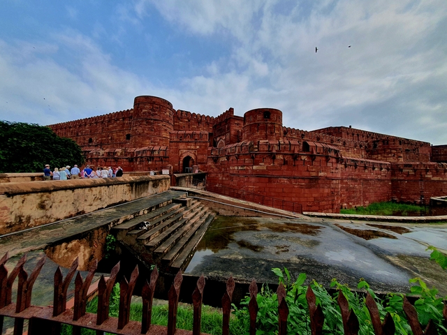       A large red fort with a group of tourists at the entrance.
  