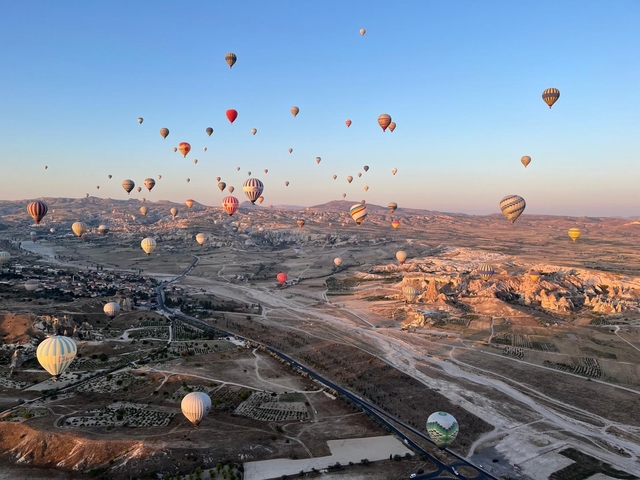A sky full of colorful hot air balloons over a landscape.