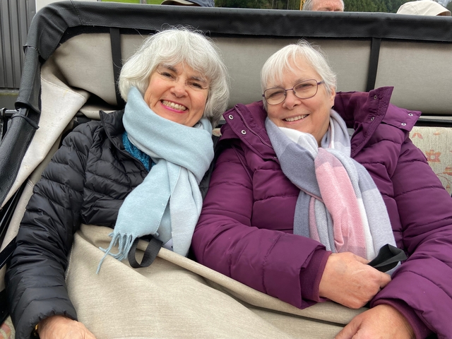       Two older women dressed warmly, sitting and smiling.
  