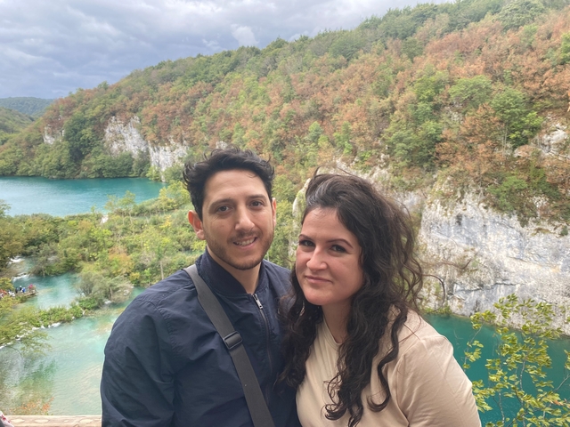       A couple in front of a scenic lake with cliffs.
  
