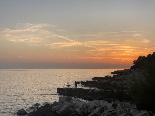       Sunset over the sea with rocky shore.
  