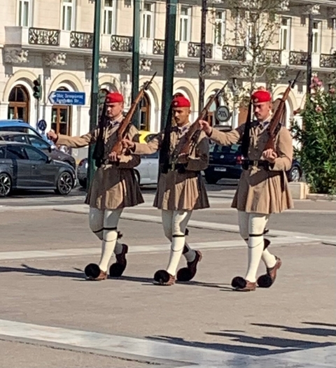       Three guards in traditional military uniforms marching.
  