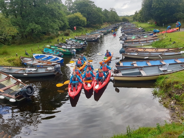       Group kayaking on a river surrounded by boats.
  