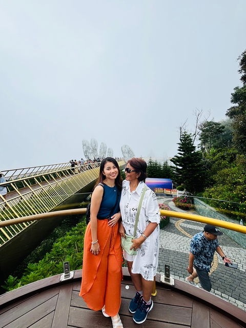       Two people on a golden bridge with misty surroundings, famous for its hand sculptures.
  