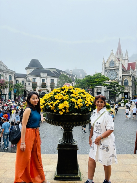       Two people by a flowerbed in a European-style village setting.
  