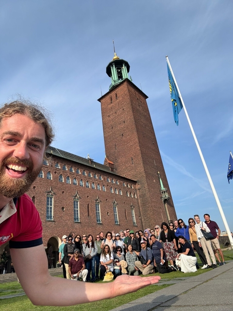 A smiling person in front of a large brick building.